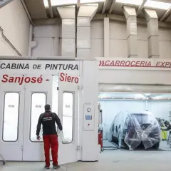 Taller de carrocería con cabina de pintura y un coche cubierto.