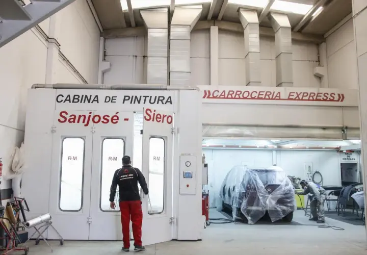Taller de carrocería con cabina de pintura y un coche cubierto.