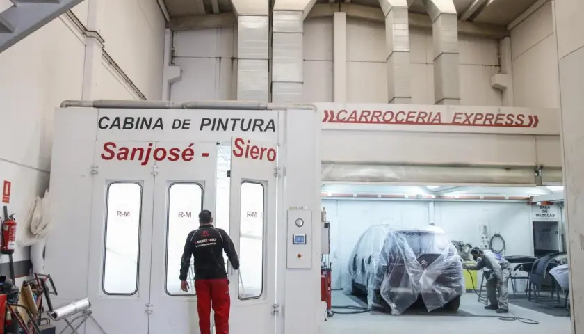 Taller de carrocería con cabina de pintura y un coche cubierto.