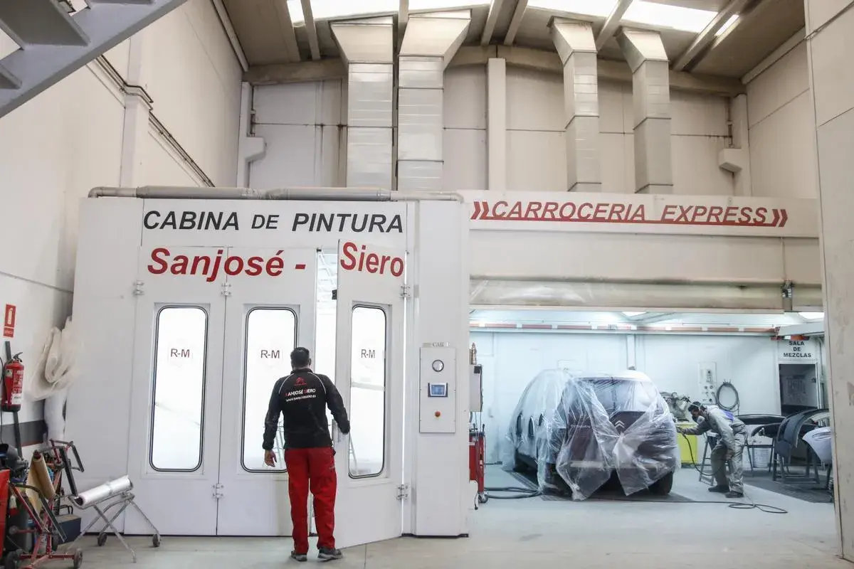 Taller de carrocería con cabina de pintura y un coche cubierto.